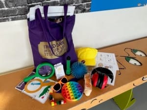 A photograph of our explorer bag, featuring items such as sunglasses, fidget toys and ear defenders